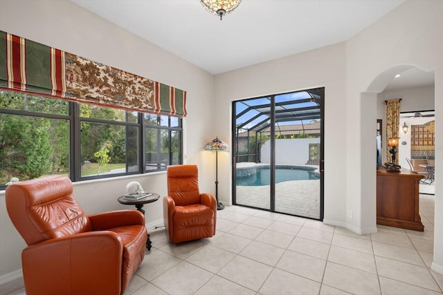 sitting room featuring light tile patterned flooring, plenty of natural light, arched walkways, and a sunroom