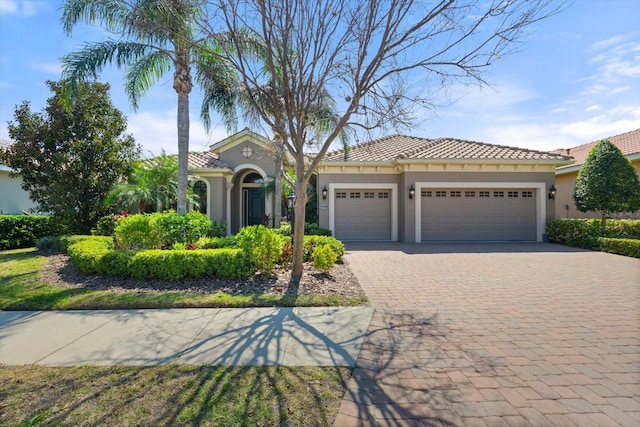 mediterranean / spanish-style house with a tiled roof, decorative driveway, a garage, and stucco siding