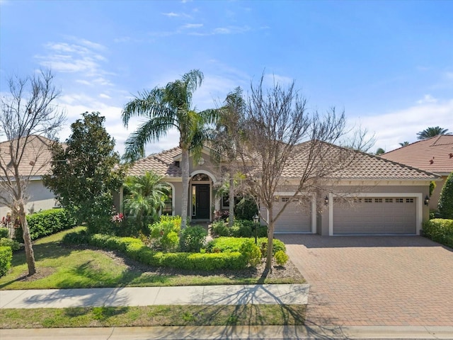 view of front of house featuring decorative driveway, a tiled roof, an attached garage, and stucco siding