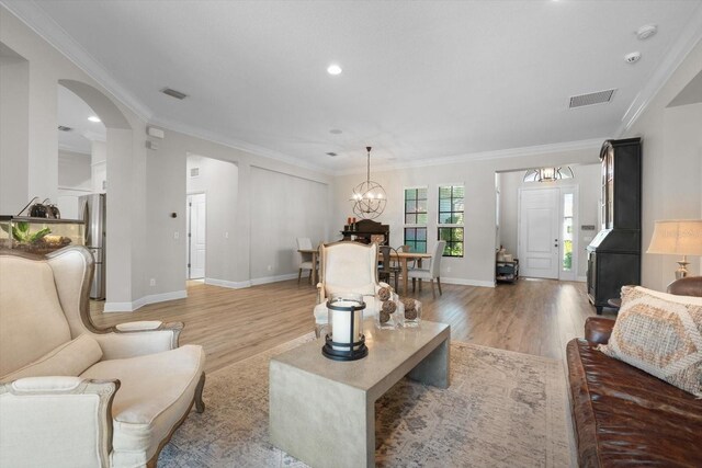 living room with visible vents, light wood finished floors, an inviting chandelier, arched walkways, and crown molding