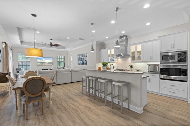 kitchen with backsplash, a breakfast bar area, appliances with stainless steel finishes, wall chimney exhaust hood, and a raised ceiling