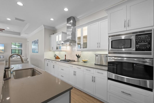 kitchen with a sink, stainless steel appliances, crown molding, wall chimney range hood, and backsplash