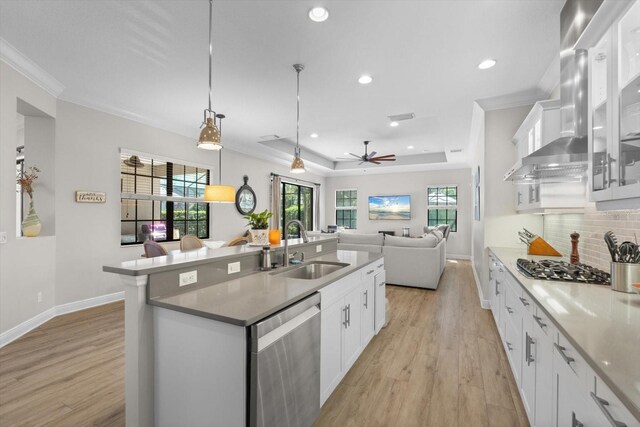 kitchen featuring a sink, stainless steel appliances, crown molding, wall chimney range hood, and backsplash