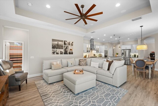 living area with a tray ceiling, visible vents, crown molding, and light wood finished floors