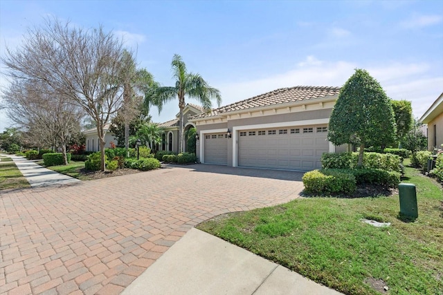 mediterranean / spanish house featuring a tiled roof, decorative driveway, an attached garage, and stucco siding