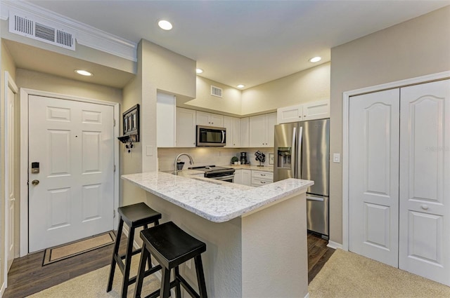 kitchen with a peninsula, white cabinets, visible vents, and stainless steel appliances