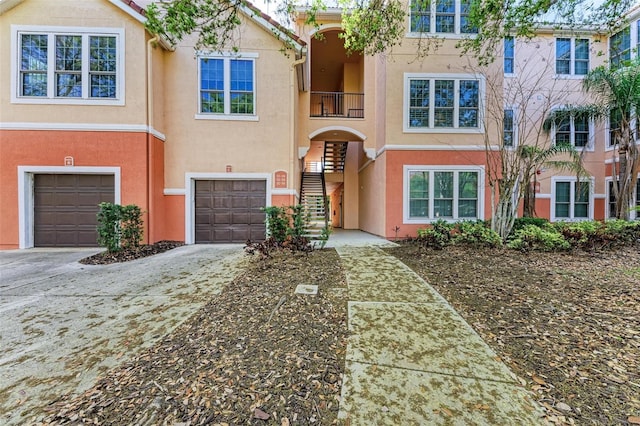 view of front facade with stucco siding, driveway, an attached garage, and stairway