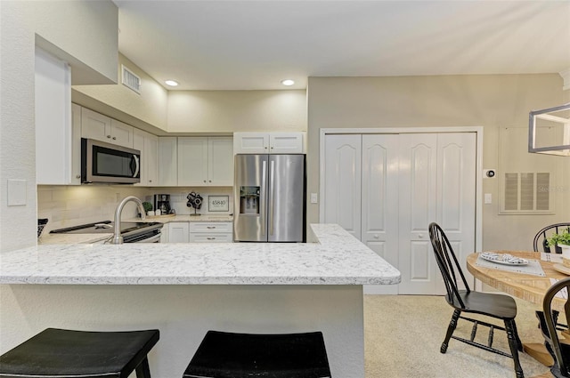 kitchen with visible vents, appliances with stainless steel finishes, a breakfast bar area, a peninsula, and decorative backsplash