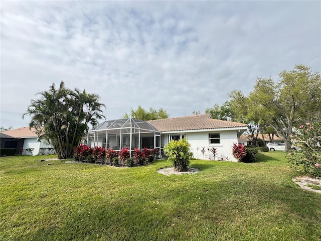 back of property with glass enclosure, a tile roof, and a yard