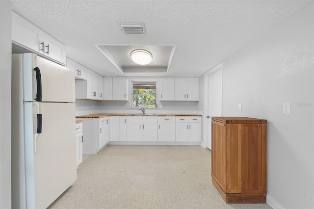 kitchen featuring visible vents, a tray ceiling, a textured ceiling, freestanding refrigerator, and white cabinets