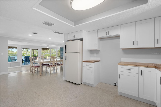 kitchen with visible vents, a tray ceiling, freestanding refrigerator, butcher block countertops, and white cabinetry