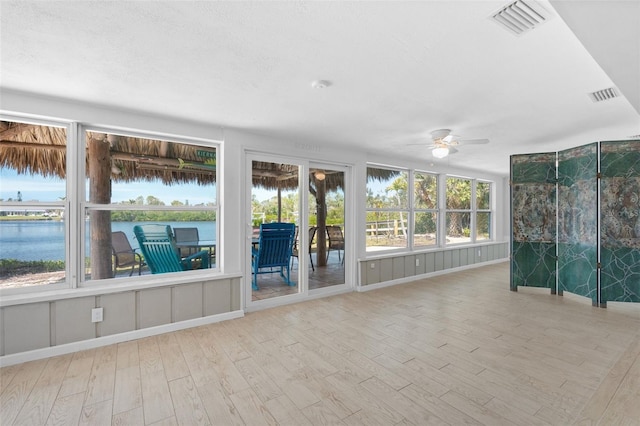 unfurnished sunroom with visible vents, a ceiling fan, and a water view