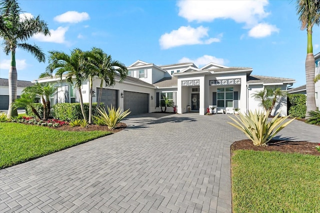 prairie-style home with stucco siding, an attached garage, decorative driveway, and a front lawn