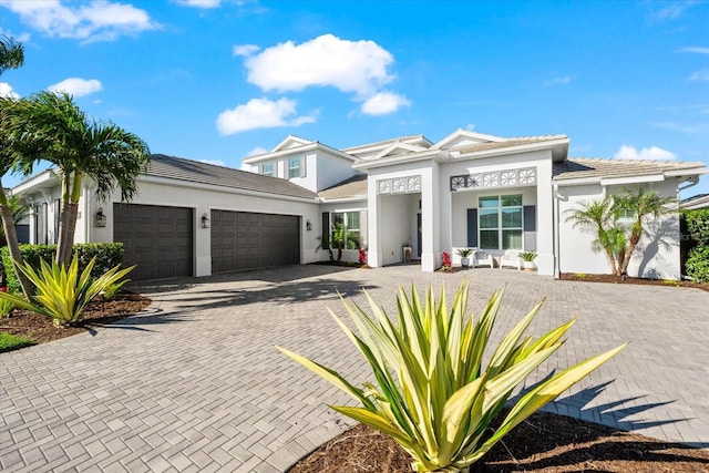 prairie-style home with stucco siding, decorative driveway, and a garage