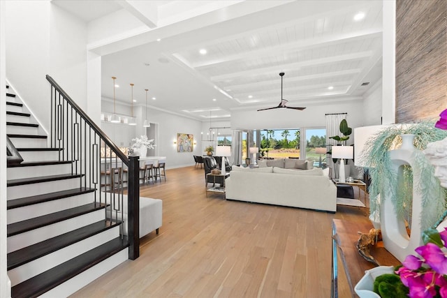 living area featuring beamed ceiling, ceiling fan with notable chandelier, hardwood / wood-style floors, baseboards, and stairs