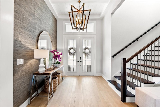 entrance foyer featuring an accent wall, a chandelier, stairs, french doors, and wood finished floors