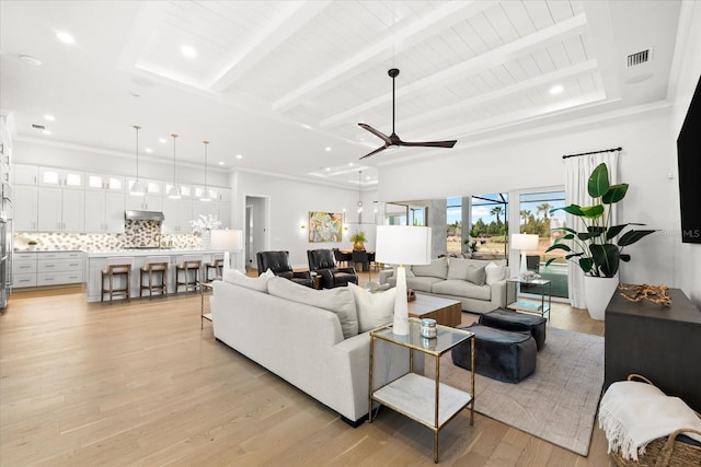 living room featuring light wood-type flooring, visible vents, beamed ceiling, and a ceiling fan