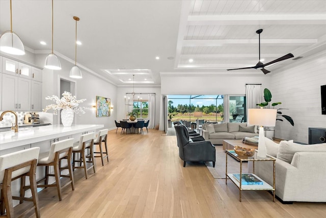 living area with light wood-type flooring, beamed ceiling, recessed lighting, crown molding, and ceiling fan