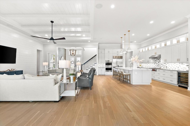 living area featuring ceiling fan, beverage cooler, beamed ceiling, stairs, and light wood-style flooring