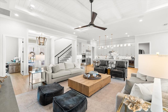 living room with visible vents, beam ceiling, beverage cooler, ceiling fan with notable chandelier, and light wood-style floors