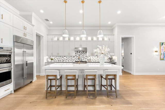 kitchen featuring a kitchen bar, under cabinet range hood, tasteful backsplash, and appliances with stainless steel finishes