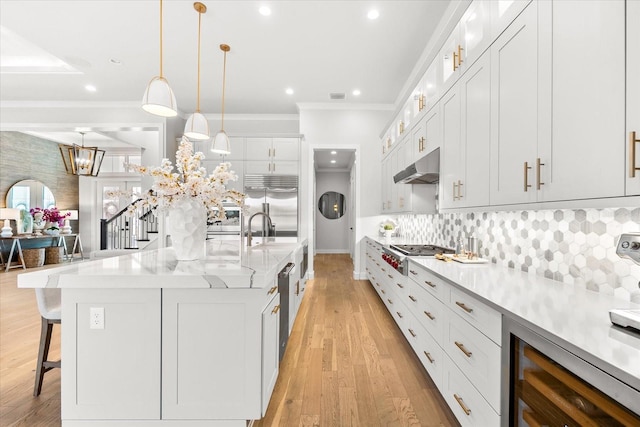 kitchen with a breakfast bar, beverage cooler, under cabinet range hood, appliances with stainless steel finishes, and crown molding