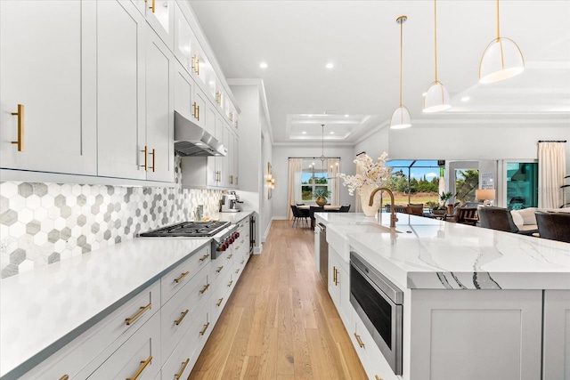 kitchen with stainless steel gas cooktop, light wood-style flooring, a large island, under cabinet range hood, and backsplash