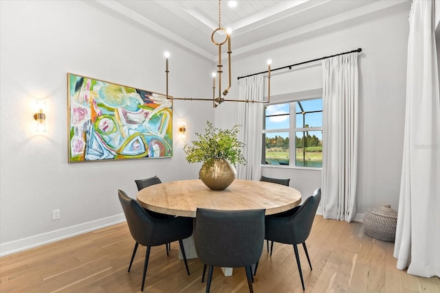 dining room featuring a notable chandelier, baseboards, a raised ceiling, and light wood-style floors