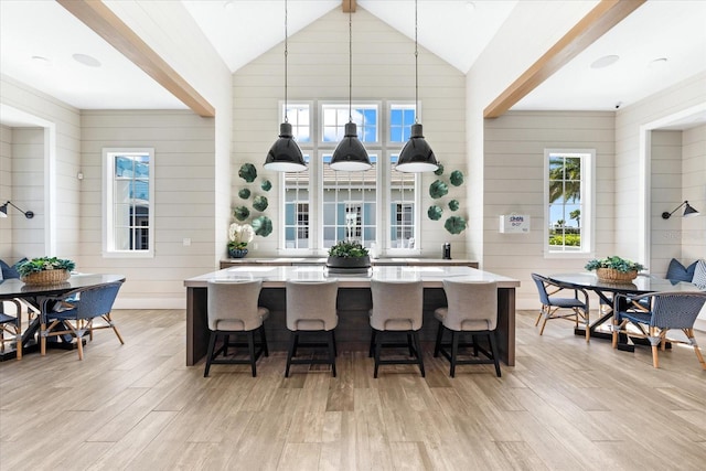 kitchen with high vaulted ceiling, a breakfast bar, decorative light fixtures, a kitchen island, and light wood finished floors