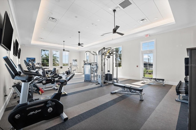 gym with a wealth of natural light, visible vents, a raised ceiling, and ceiling fan