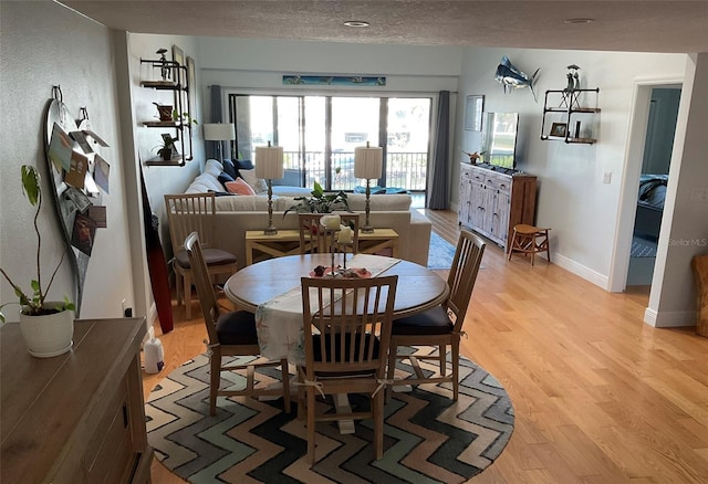 dining space with baseboards, a textured ceiling, and light wood-style floors