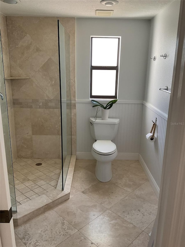 full bathroom featuring a textured ceiling, toilet, a wainscoted wall, and a stall shower