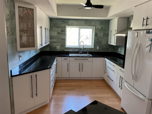 kitchen featuring dark countertops, wall chimney range hood, light wood-type flooring, freestanding refrigerator, and a sink