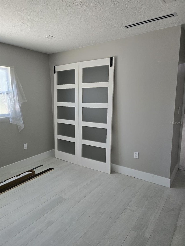 unfurnished room with baseboards, wood finished floors, visible vents, and a textured ceiling