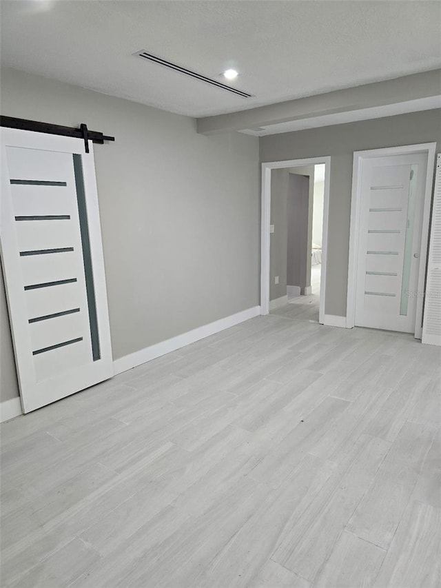 spare room with light wood finished floors, visible vents, baseboards, and a barn door