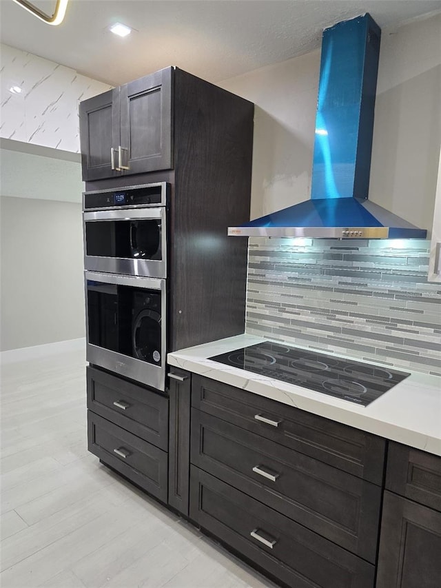 kitchen with black electric stovetop, tasteful backsplash, light countertops, and wall chimney range hood