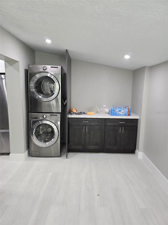 clothes washing area featuring cabinet space, a textured ceiling, stacked washing maching and dryer, and baseboards