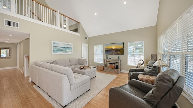 living room featuring visible vents, a high ceiling, a fireplace, light wood finished floors, and baseboards