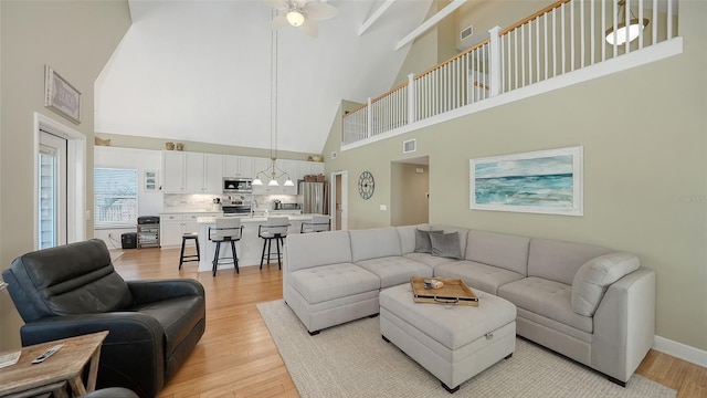 living room with baseboards, a high ceiling, a ceiling fan, and light wood finished floors