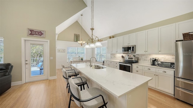 kitchen with a breakfast bar area, a kitchen island with sink, a sink, stainless steel appliances, and white cabinets