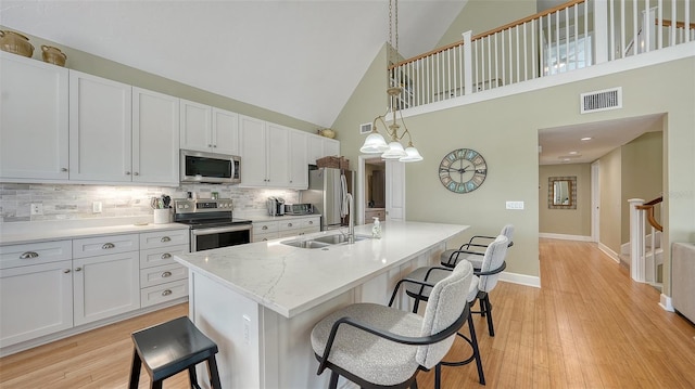 kitchen with light wood-type flooring, visible vents, stainless steel appliances, a breakfast bar area, and white cabinets