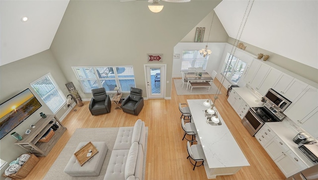 living area featuring a notable chandelier, light wood-style flooring, high vaulted ceiling, and baseboards