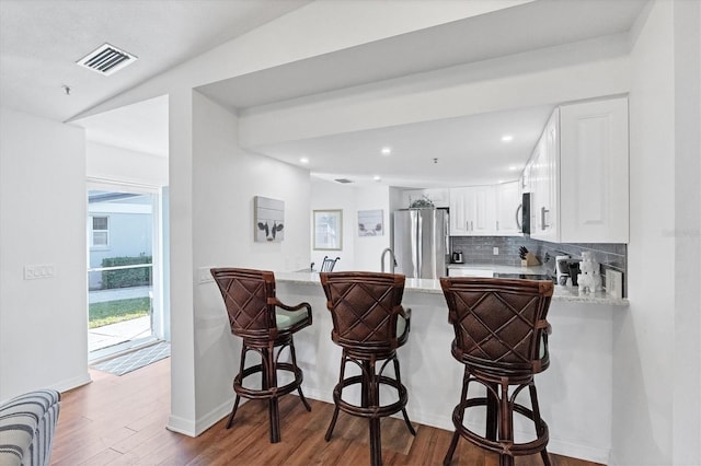 kitchen featuring visible vents, wood finished floors, appliances with stainless steel finishes, a peninsula, and decorative backsplash