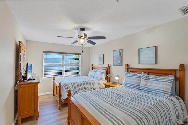 bedroom featuring baseboards, visible vents, a textured ceiling, and light wood-style floors