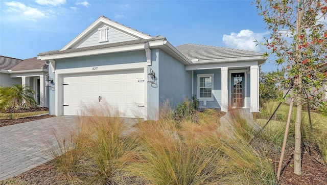 ranch-style home featuring stucco siding, an attached garage, a tile roof, and decorative driveway