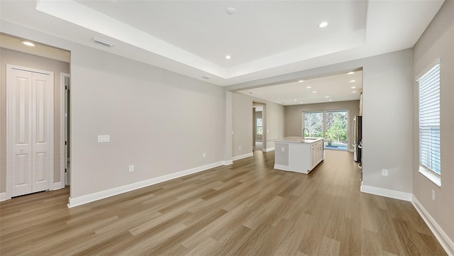 unfurnished living room with visible vents, baseboards, light wood-type flooring, and a tray ceiling