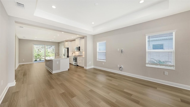 unfurnished living room with a raised ceiling, a sink, wood finished floors, recessed lighting, and baseboards