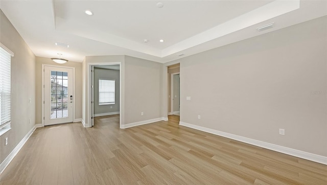 empty room with light wood finished floors, visible vents, baseboards, and a tray ceiling