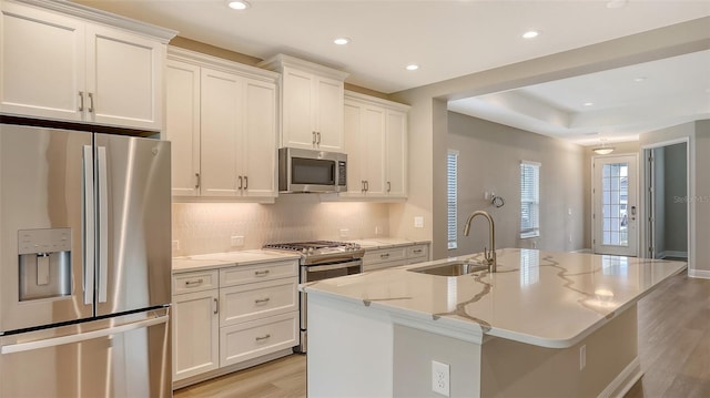 kitchen featuring backsplash, a center island with sink, appliances with stainless steel finishes, light wood-style floors, and a sink