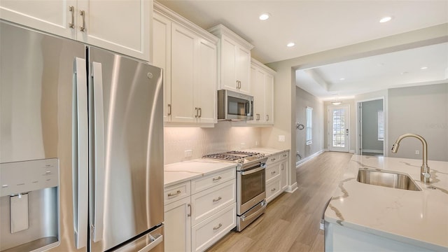 kitchen featuring light wood-style flooring, a sink, stainless steel appliances, white cabinets, and tasteful backsplash